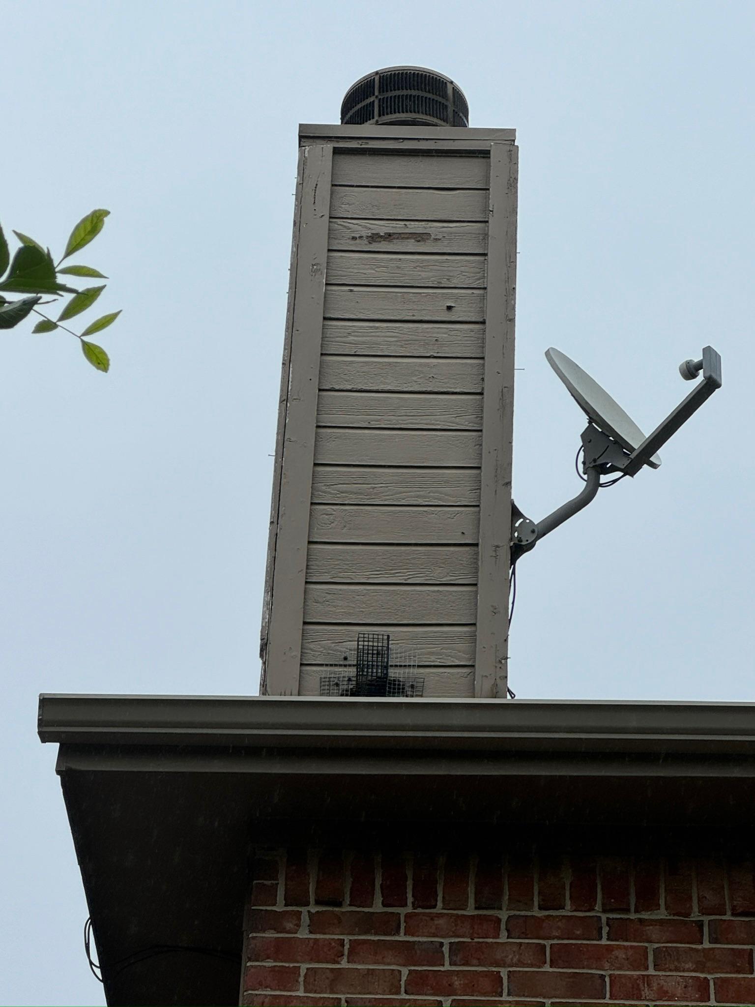 Tall siding-clad chimney with a chimney cap above a brick home