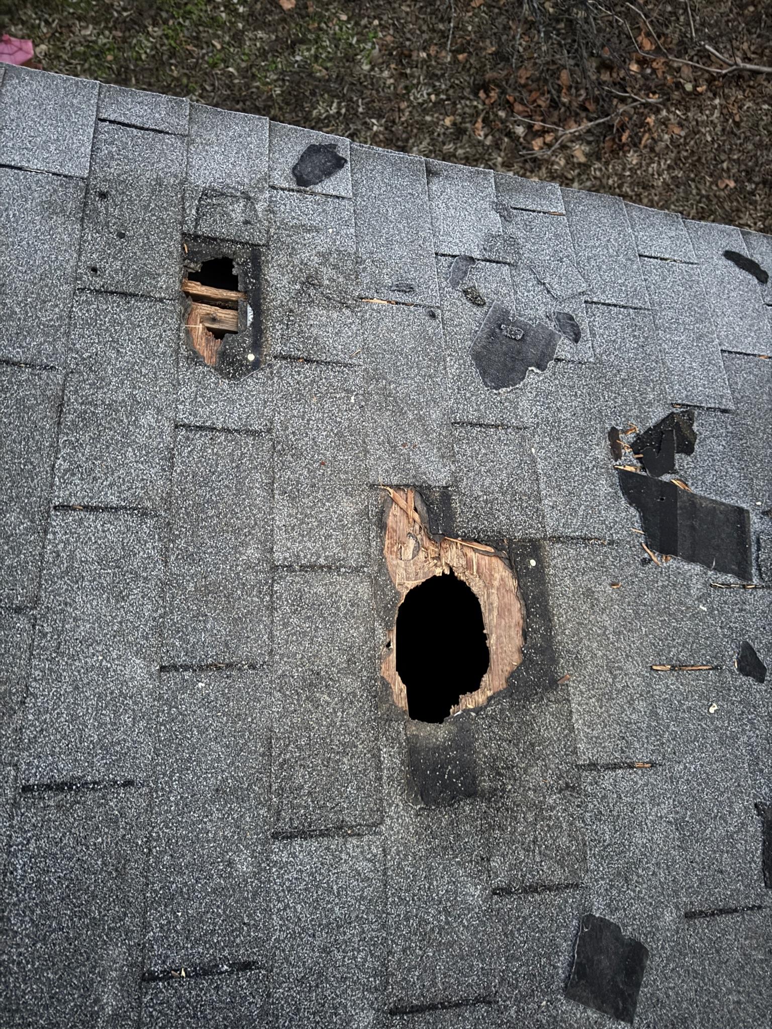 Large hole in shingles and roof decking near a smaller damaged patch