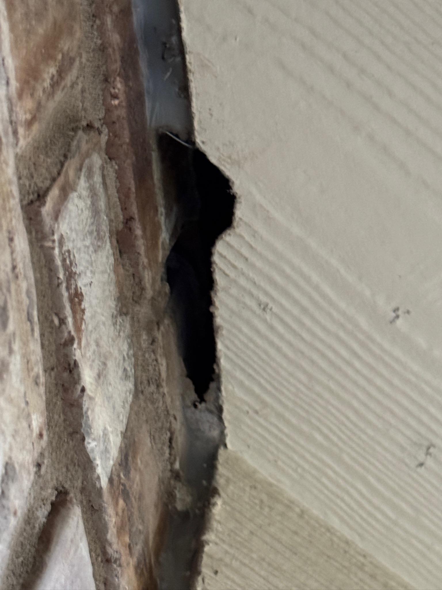 Dark vertical opening between brickwork and exterior siding