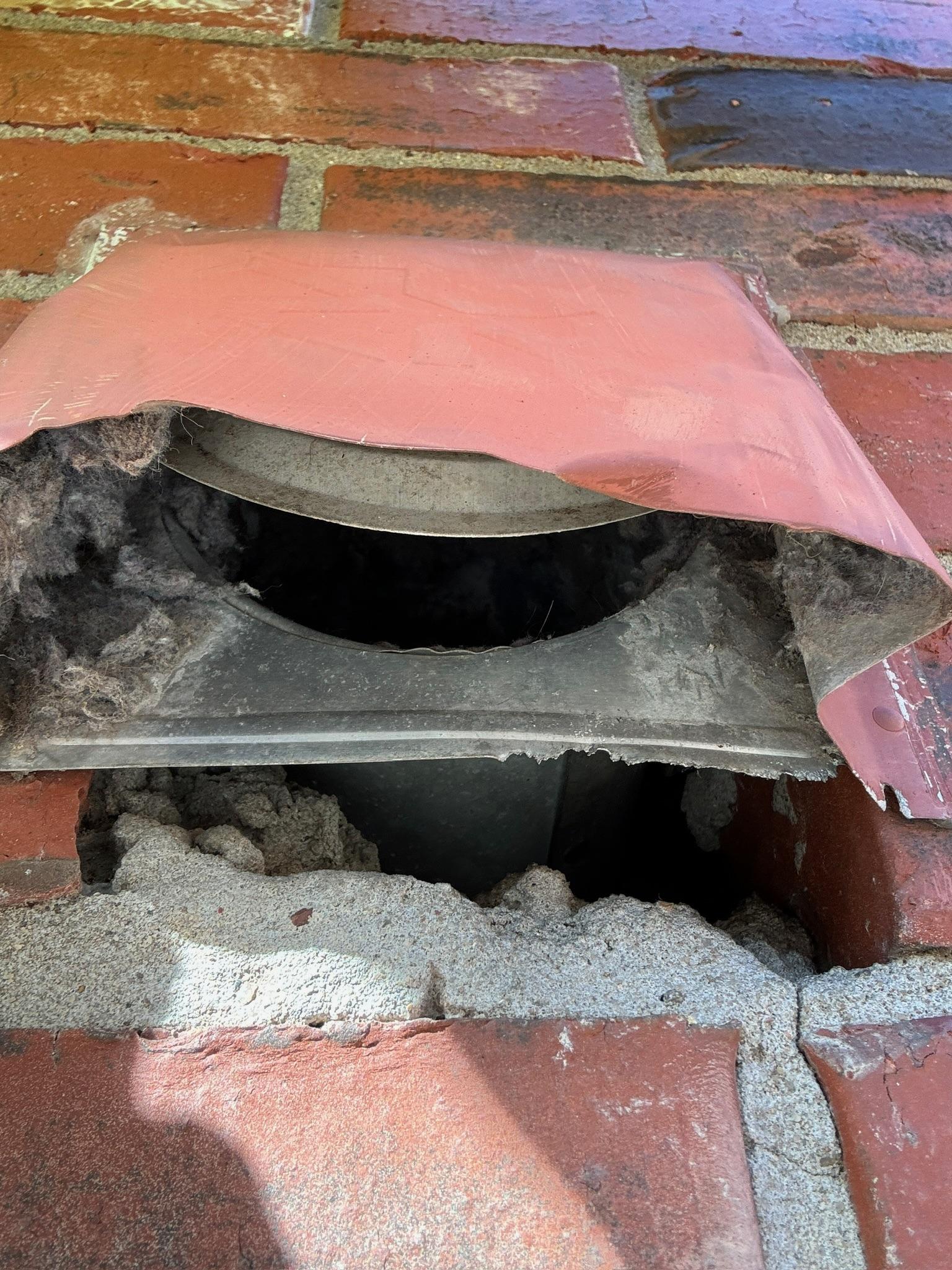 Damaged vent cover exposing an opening in a brick wall